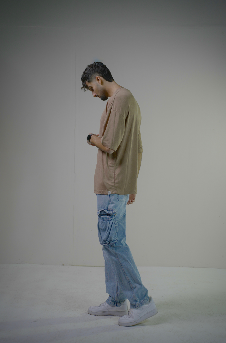 Man wearing a beige long-sleeve shirt and light blue jeans standing against a plain background
